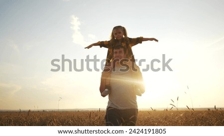 the child sits on father shoulders. happy life and family for child concept. little girl spreads her arms to the sides and sits on her father shoulders, a man walks lifestyle through the field