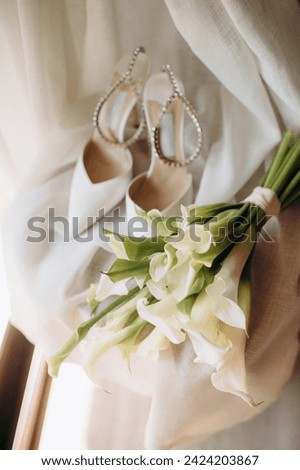 A close-up shot of a detail of the bride's clothing, a modern composition of stylish wedding accessories, high-heeled shoes, a modern bridal bouquet of white flowers. Wedding preparations Royalty-Free Stock Photo #2424203867