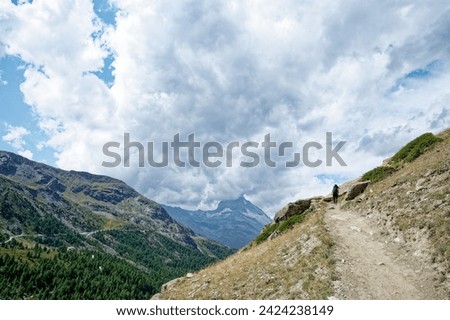 solo female hiker traverses a dirt path on the 5-lake journey, with the iconic Matterhorn veiled in dense clouds.