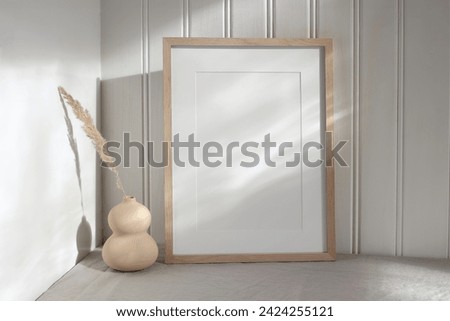 Blank vertical picture frame mock up in sunlight. Modern vase with dry grass festuca. White wooden wall background with floral shadows. Neutral Scandinavian home decor, nordic interior.