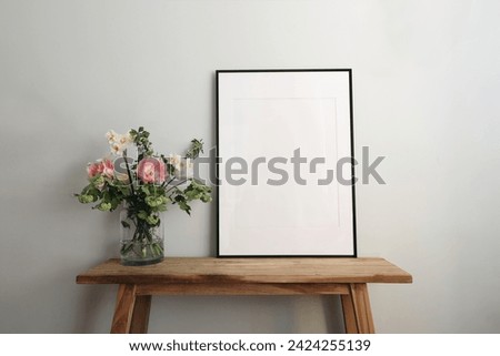 Easter springtime still life. Blank black picture frame mockup on wooden bench, table. Spring bouquet of pink tulips, white daffodils, hawthorn flowers, pastel green, mint wall background.