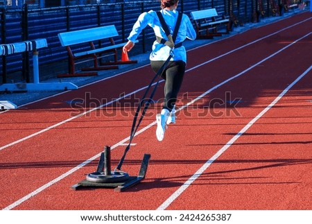 Rear view of a high school girl running on a track pulling a sled with weight.