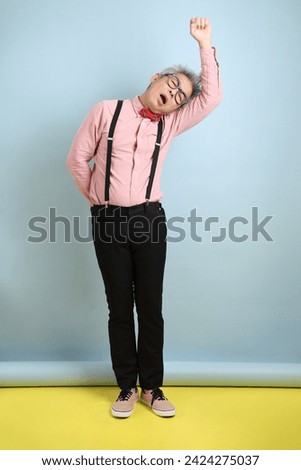 Asian senior man in black suspenders with red bow with gesture of Waiting isolated on blue background. St Valentine's Day