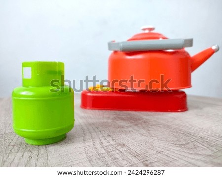 Isolated toy 3 kg green Liquefied Petroleum Gas (LPG) gas cylinder for cooking water in a teapot on wooden and white background