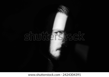 A man stands in the dark and a beam of light illuminates part of his face. Black background. Art photography. Psychological picture. Copy space.
