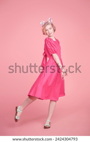 Teenage and kids Fashion. A modern teen girl with a short blonde hair with orange streaks poses with flower stickers on her face, wearing a pink dress. Pink background. Gentle spring-summer look.
