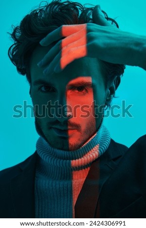 Portrait of a handsome brunette man with curly hair posing in blue lighting with a red stripe light. Color, fashion and style. Art Fashion photo.