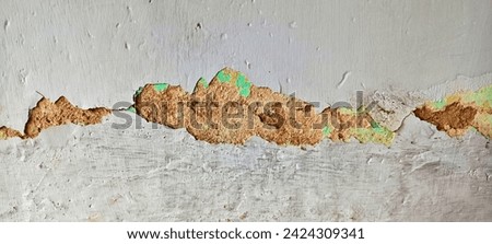 A close-up of a cracked and peeling concrete wall. The wall is painted white, but the paint is peeling away in large flakes. The cracks in the wall are large and deep. Royalty-Free Stock Photo #2424309341