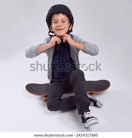 Smile, skateboard and portrait of child in studio with helmet for safety learning skating. Happy, security and young boy kid with headgear for practicing fun hobby or activity by gray background. Royalty-Free Stock Photo #2424317685