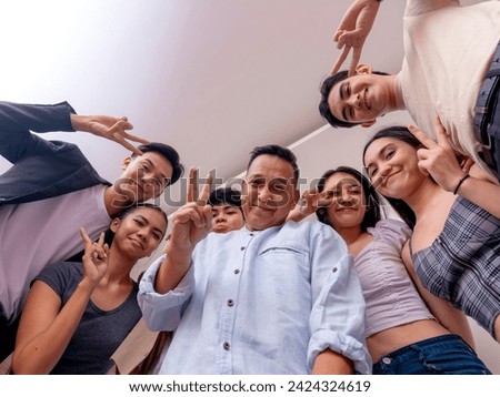 6 young interns posing with their boss. Low angle shot making peace gestures. Startup company showing solidarity and unity.