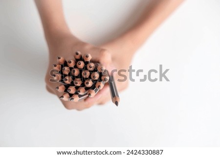 Closeup shows 25 pencils in a child's hand on a white table. focus is on the tips of the pencils, which are sharpened and ready for use. This image represents the importance of education 