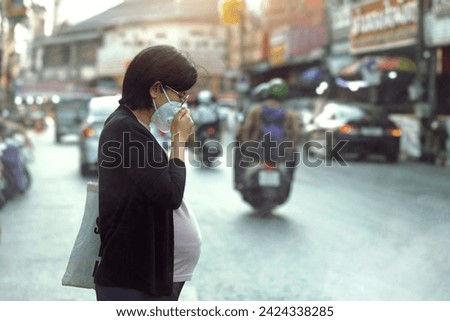 Asian pregnant woman in the middle of the road wears a PM2.5 dust mask to protect against pollution, anti smog and viruses, Air pollution causes a health problem. City air pollution concept. Royalty-Free Stock Photo #2424338285