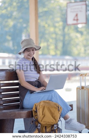 Young Asian woman girl works with a laptop in the train station, Young woman with travel bag sitting on couch using laptop for work, Young freelance working at the train station before travel.