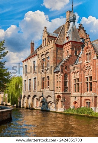 Medieval town Bruges in Belgium. Panorama and landscape vintage channel with old bruges brick houses broach on roof. Sunny day Brugge blue sky, clouds green trees. Europe travel destination. Royalty-Free Stock Photo #2424351733