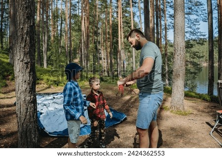 caucasian man putting up a tent in pine forest. Children helping him. Family camping concept. High quality photo