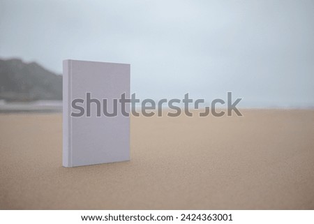 Book with a white cover without texts or drawings in the sand of the beach on a cloudy day. Royalty-Free Stock Photo #2424363001