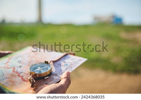 Close-up tourist's hand holds a compass with magnetic arrow showing north direction, over a map against lighthouse background. Copy advertising space. People and travel. Tourism. Adventure. Hiking
