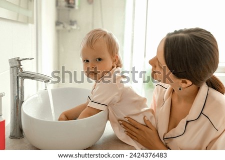 Mother watching daughter brushing teeth at home. Happy woman brushing teeth with her daughter. Little girl brushing teeth with her mom. Good morning concept. Daily routine and health care