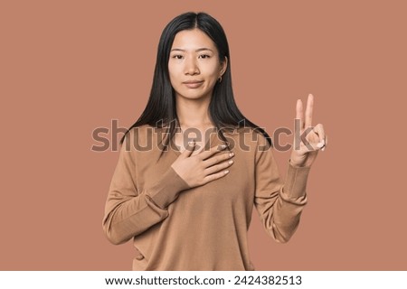 Young Chinese woman in studio setting taking an oath, putting hand on chest.