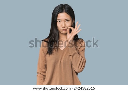 Young Chinese woman in studio setting with fingers on lips keeping a secret.