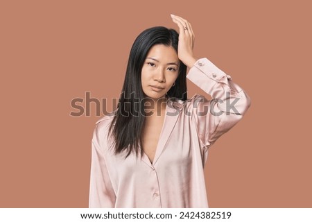 Young Chinese woman in studio setting tired and very sleepy keeping hand on head.