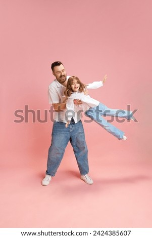 Full length portrait of young man, father playing with child, little girl against pink studio background. Concept of International Day of Happiness, childhood and parenthood, positive emotions. Ad