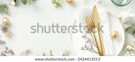 Easter table decorations. Stylish Easter brunch table setting with white plate, napkin, golden cutlery, easter eggs and spring branches on light grey background top view flat lay copy space