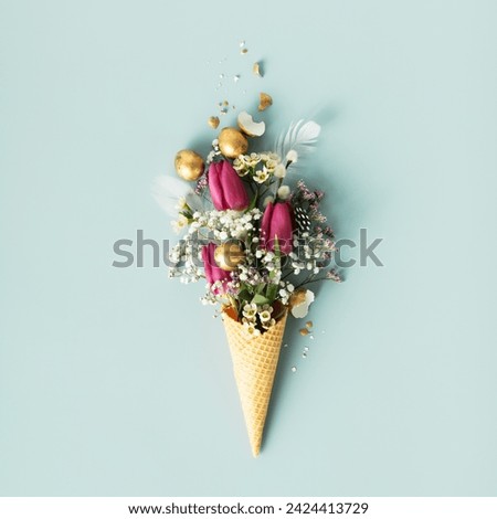 Easter composition. Ice cream cone with beautiful flowers and golden easter eggs on blue background flat lay