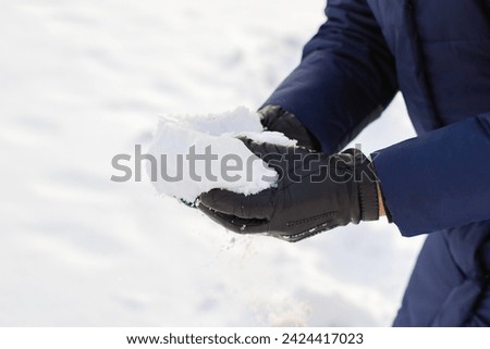 pile of snow in hands after heavy snowfall. man in gloves and winter clothes takes snow in his hands. leisure activities, snowball fight game