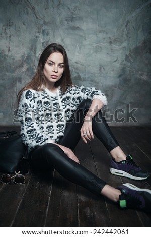 Portrait of beautiful girl in the studio in fashionable clothes sitting on the floor