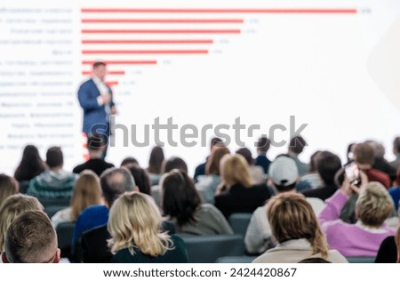 Blurred speaker engaging audience during a conference presentation in a modern venue.
