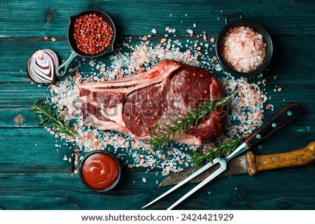Raw Beef Aged Steak on the Bone with Rosemary, Sea Salt and Spices. On a blue wooden background. Top view.