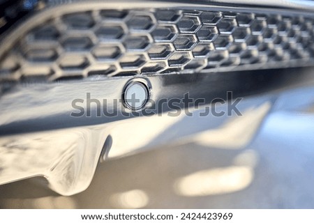 Selective focus on left side of rear bumper parking sensor at back of luxurious car bumper close up on grid background with copyspace.