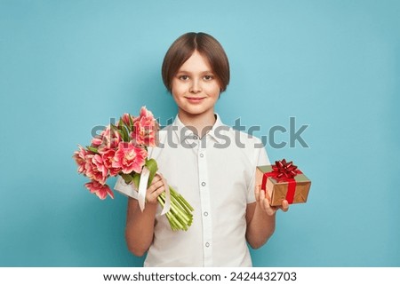 Cheerful happy child with Tulips bouquet and present. Smiling boy on blue background, rejoices spring holiday. Women's Day on March 8th