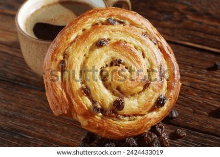 Puff pastry raisin bun and cup of coffee on the table close-up. Shallow depth of field