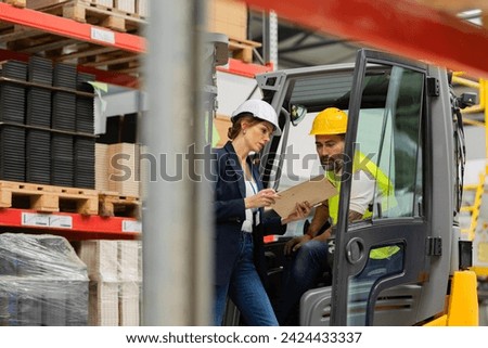 Forklift driver talking with manager in modern industrial factory. Warehouseman reading order, order picking. Warehouse worker preparing products for shipmennt, delivery, checking stock in warehouse.