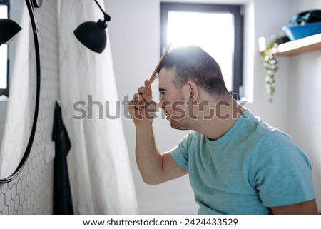 Young man with down syndrome in bathroom, combing his hairs. Royalty-Free Stock Photo #2424433529