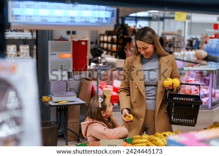 Smiling young mother and daughter picking fresh fruits and vegetables in grocery store.