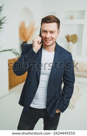 A young smiling man in a jacket is talking on the phone. Emotions of laughter from talking on the phone. A successful man works remotely on the phone.