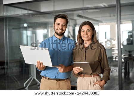Two business partners executives standing in office looking at camera. 2 sales managers, company agents, consultancy professionals, bank advisors with devices posing for corporate portrait. Royalty-Free Stock Photo #2424450085