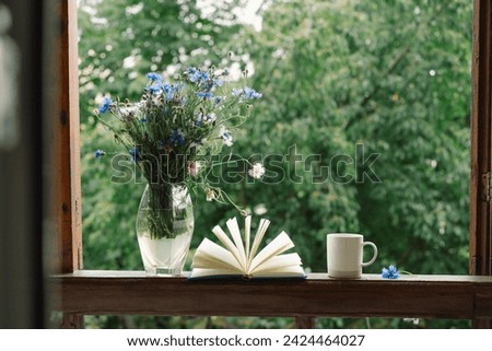 Beautiful summer still life on the windowsill. A bouquet of cornflowers and a book on the windowsill in a cozy home. Royalty-Free Stock Photo #2424464027