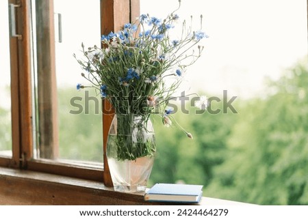 Beautiful summer still life on the windowsill. A bouquet of cornflowers and a book on the windowsill in a cozy home.