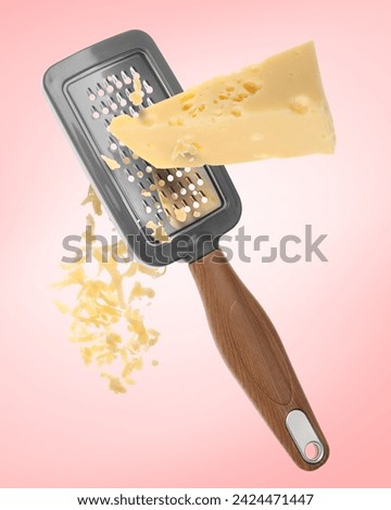 Grating cheese with hand grater on pink background Royalty-Free Stock Photo #2424471447
