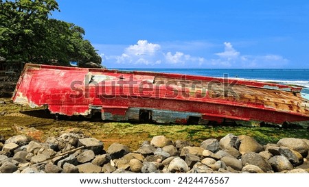 A red shipwreck drifting in a storm. A big blue sky with white clouds fills the background and a rocky beach is in the foreground.close up angle