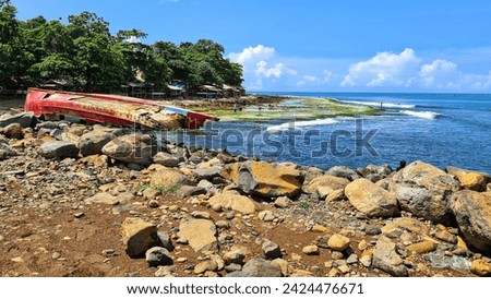 A red shipwreck drifting in a storm. A big blue sky with white clouds fills the background and a rocky beach is in the foreground.