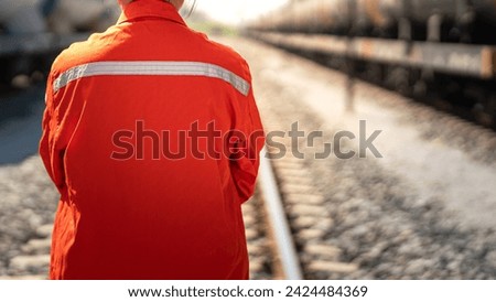 Close-up at back of a worker in safety uniform suit with reflection sight bar, standing on the train locomotive and railway track as background. Ready to working in transportation industrial concept. Royalty-Free Stock Photo #2424484369