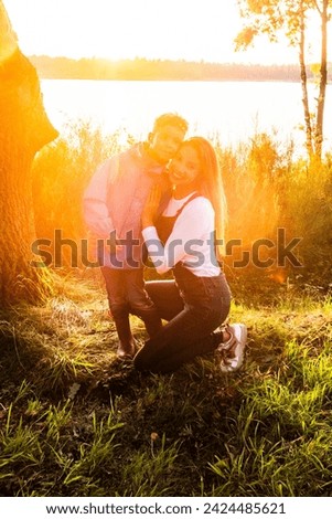 In this heartening photograph, a mother kneels to hug her child in a loving embrace, surrounded by the natural beauty of a lakeside at sunset. The golden sunlight bathes the scene, creating a halo