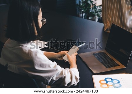 Back view of skilled female using cellphone technology at table desktop with modern laptop computer and touch pad, millennial woman connecting to 4g wireless on smartphone for browsing website