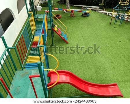 children's play area with slides and colorful suspension bridges. children's playground with green synthetic grass carpet Royalty-Free Stock Photo #2424489903