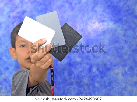 boy posing with set of 3 cards white, gray and black for determining the exact white balance on his hand